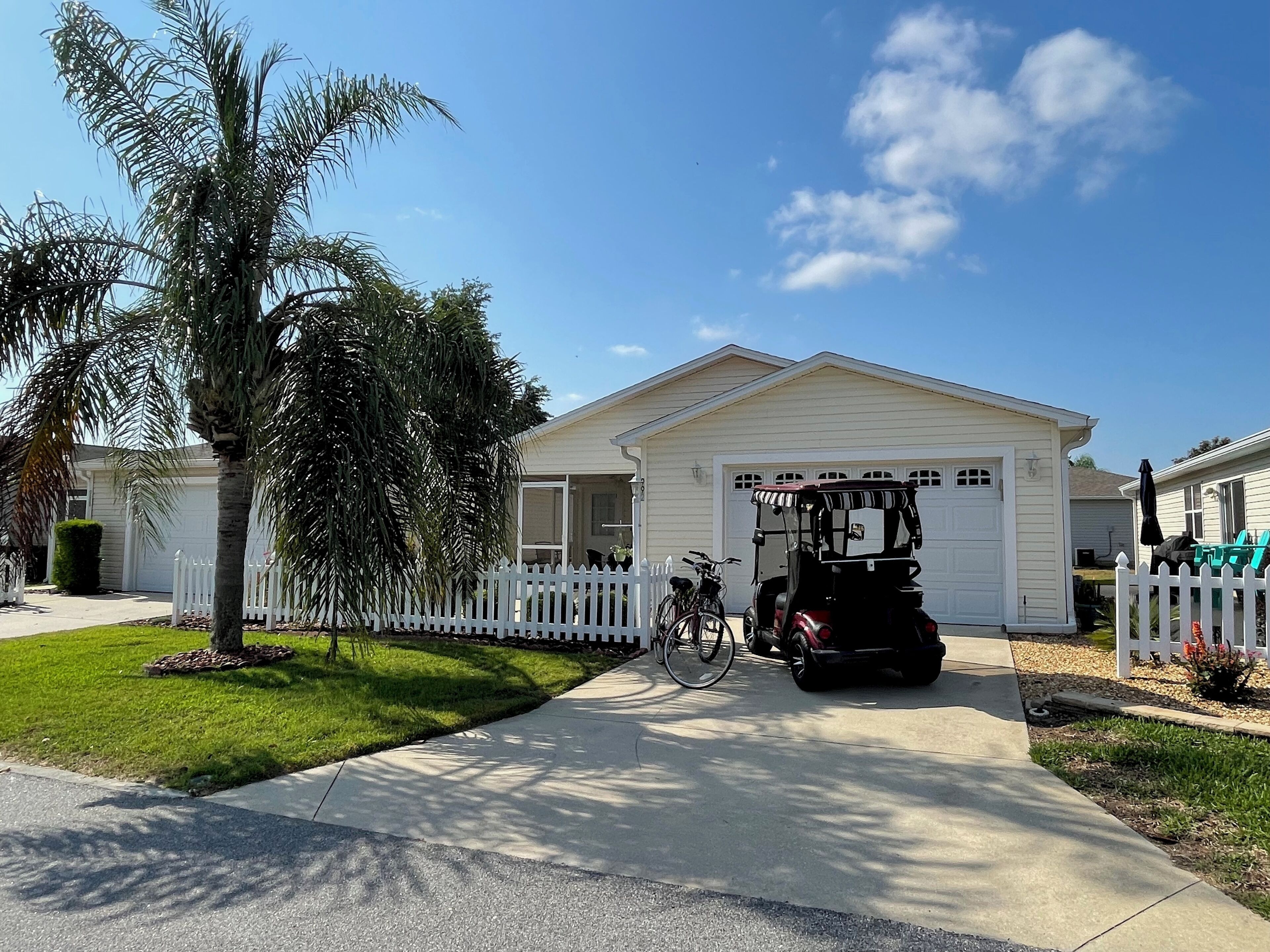 A single-story house with a garage, a white picket fence, and a golf cart parked in front.