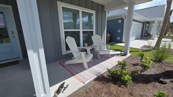 A house with a porch, two Adirondack chairs, and a small table.