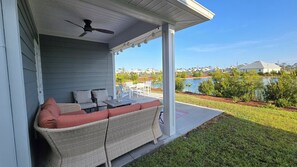 A covered porch with outdoor furniture, a ceiling fan, and a view of a lake and neighborhood houses.