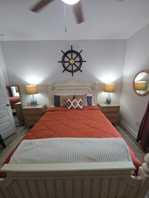 A bedroom with a bed, two bedside tables, a wall-mounted ship's wheel, and a mirror.