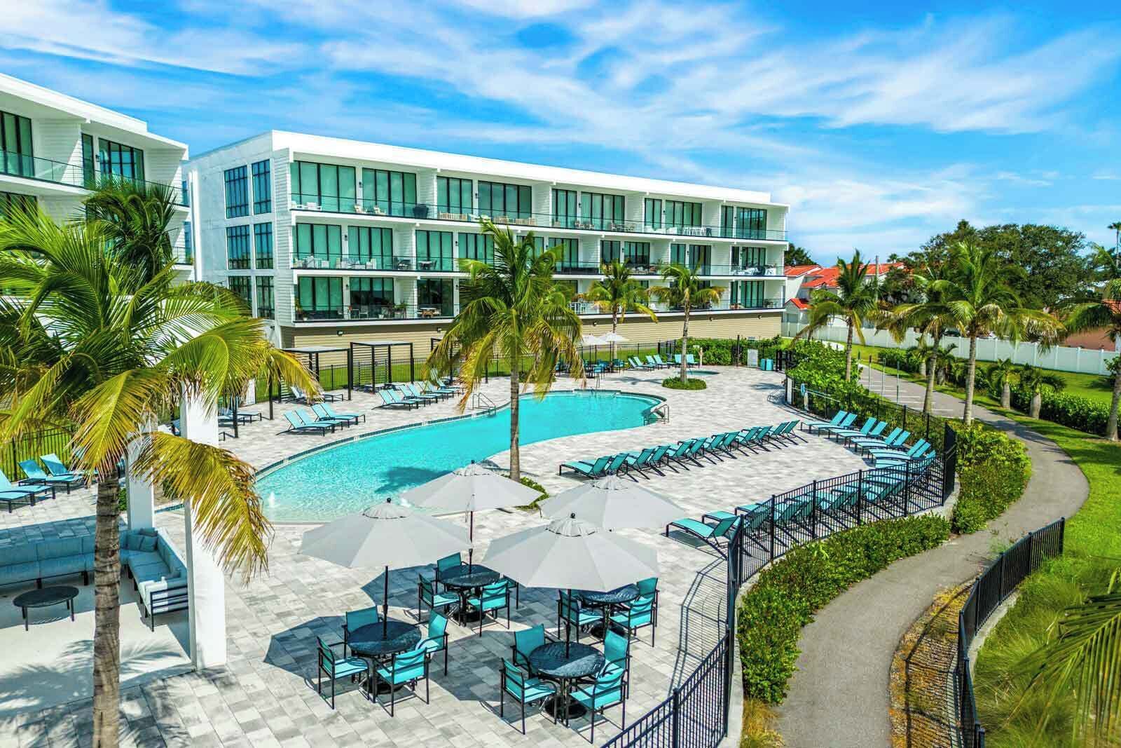 Ein modernes Hotel mit Poolbereich, Sitzgelegenheiten im Freien und Palmen.
