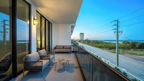 Un balcon avec un canapé, deux petites tables et une vue sur l’océan et la route.