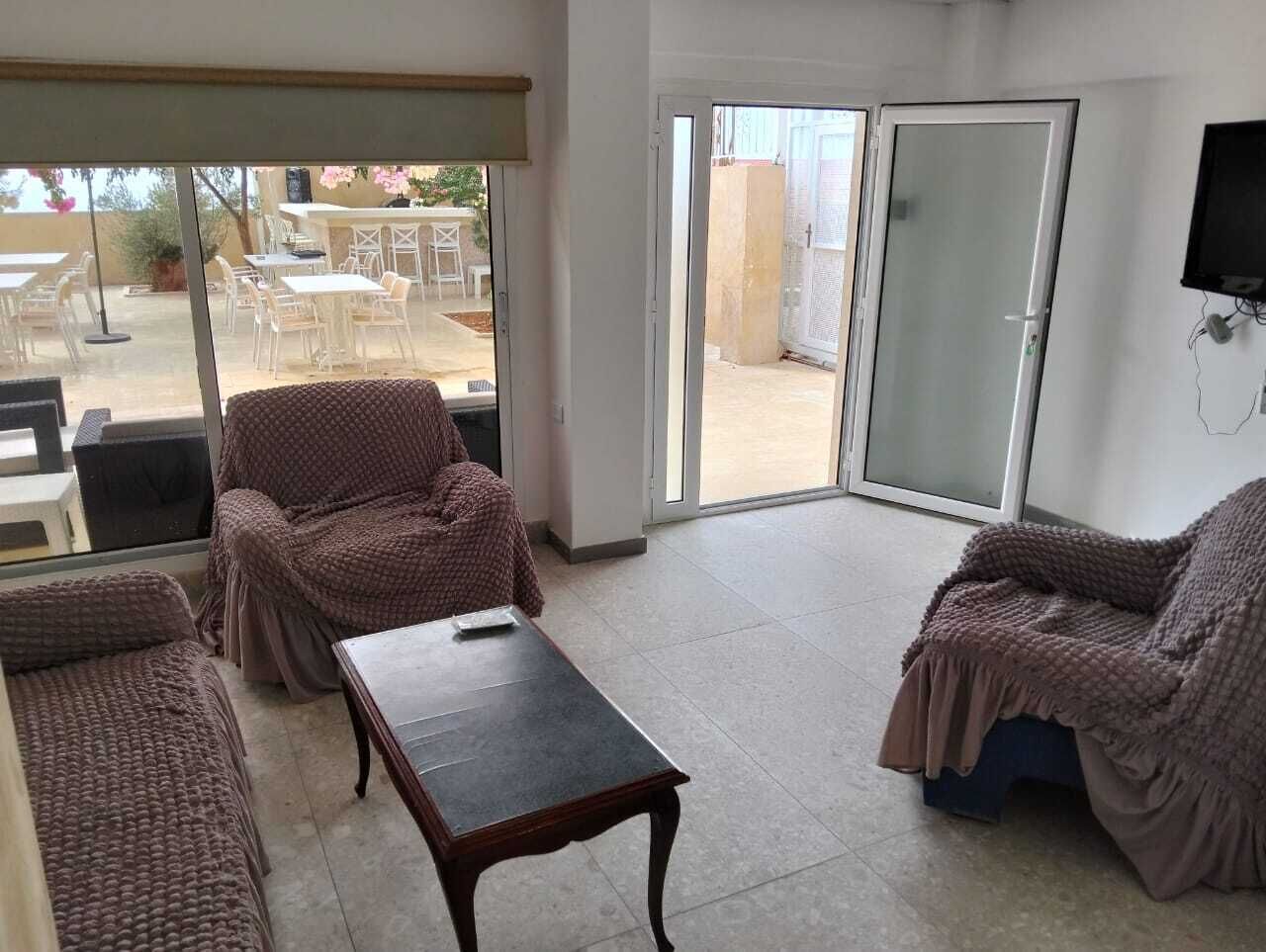 Amplia sala de estar con un gran ventanal corredero que da a un patio exterior. Hay dos sillones acolchados y una pequeña mesa.