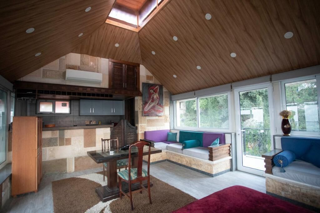 Een ruime loft met hoge plafonds, een keukenhoek, een eettafel en een zithoek met grote ramen.