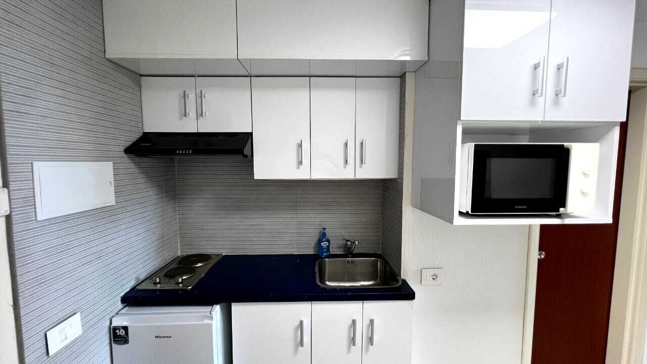 Une cuisine de taille réduite avec des meubles blancs, une cuisinière noire, un four à micro-ondes et un évier.