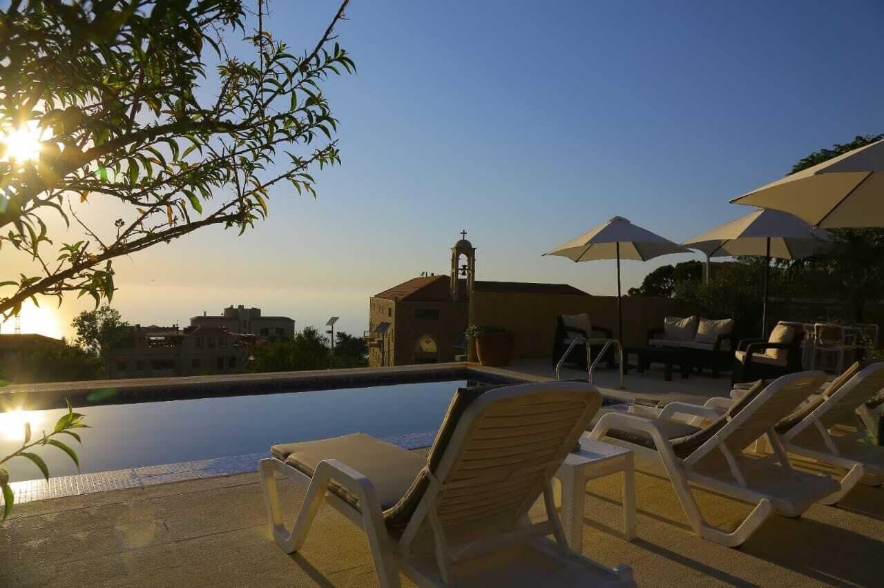 A swimming pool with lounge chairs and umbrellas, a bell tower, and a clear sky.