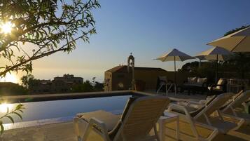 A swimming pool with lounge chairs and umbrellas, a bell tower, and a clear sky.