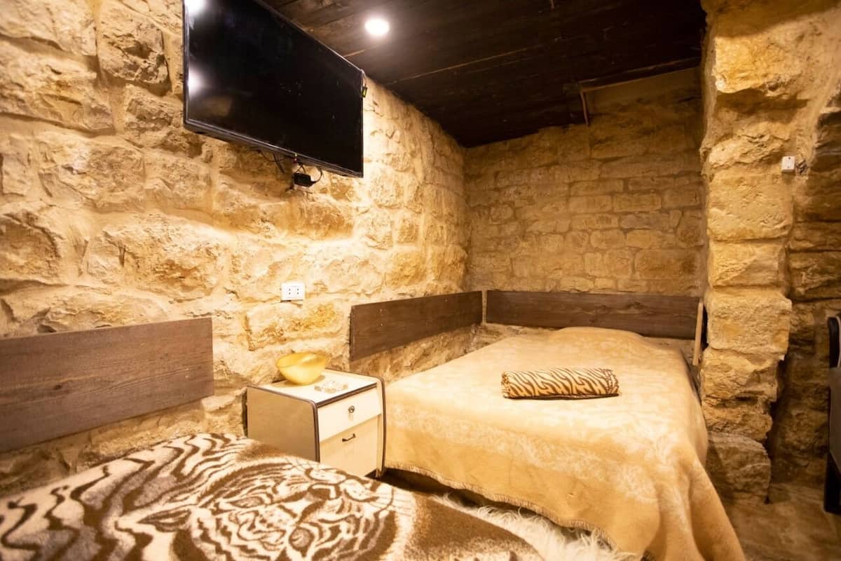 A stone-walled room with a bed, a nightstand, a television, and a wooden headboard.