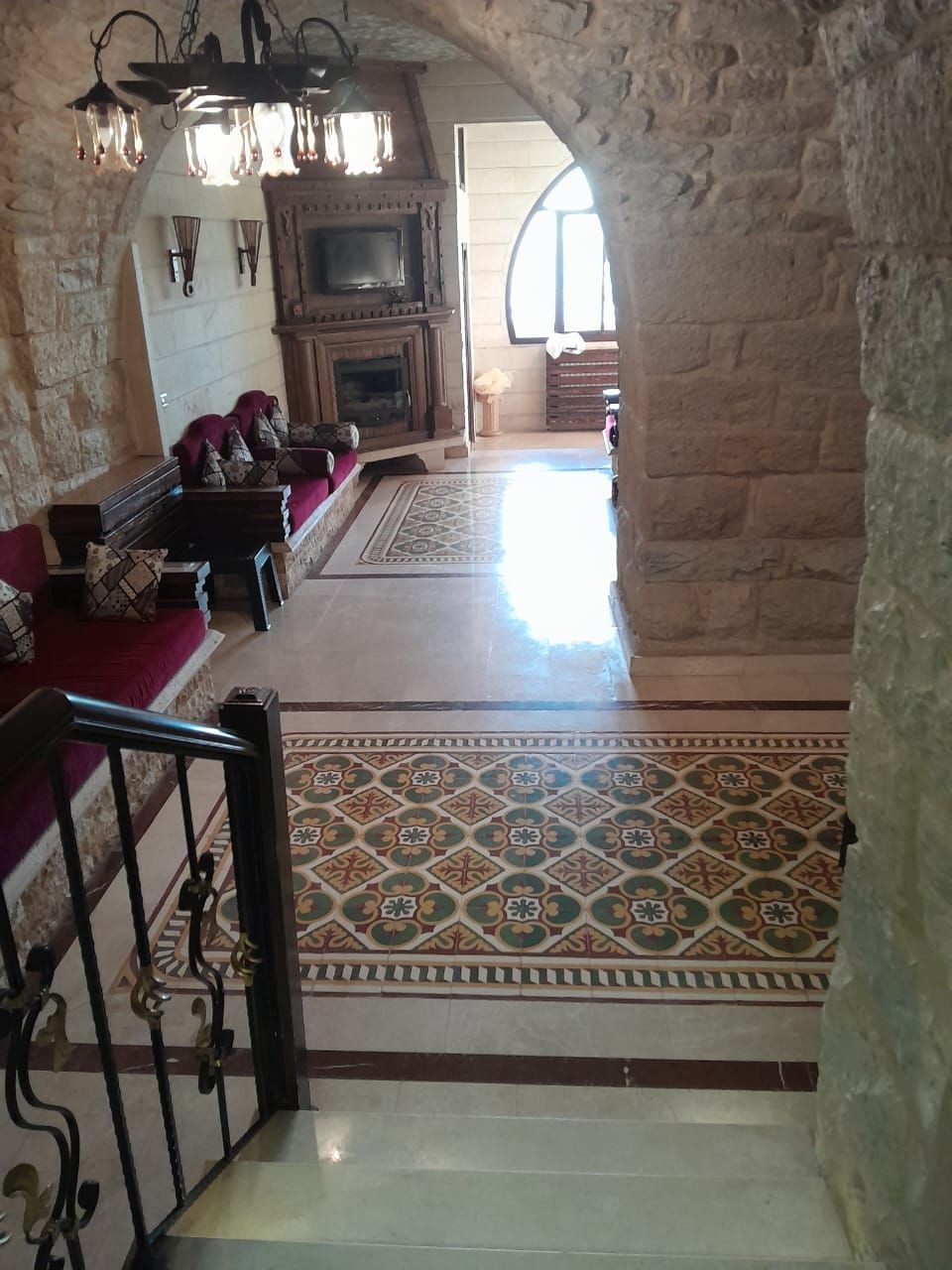Ein Zimmer mit Steinwänden, einem Kamin, einem gemusterten Teppich und einer Treppe, die zu einer anderen Ebene führt.