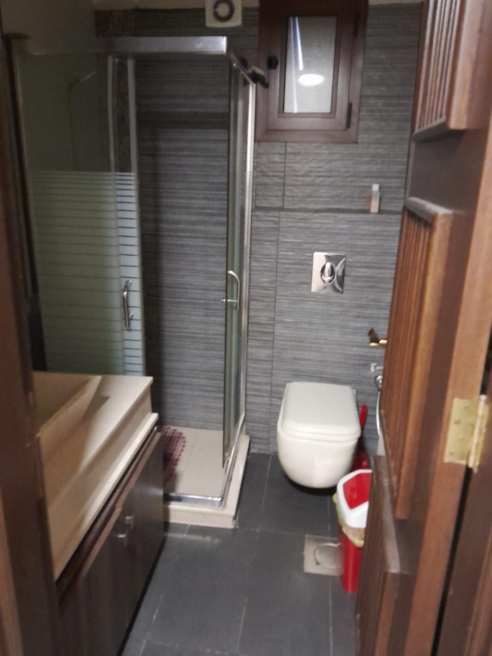 Casa de banho compacta com cabine de duche em vidro, sanita branca e lavatório pequeno.