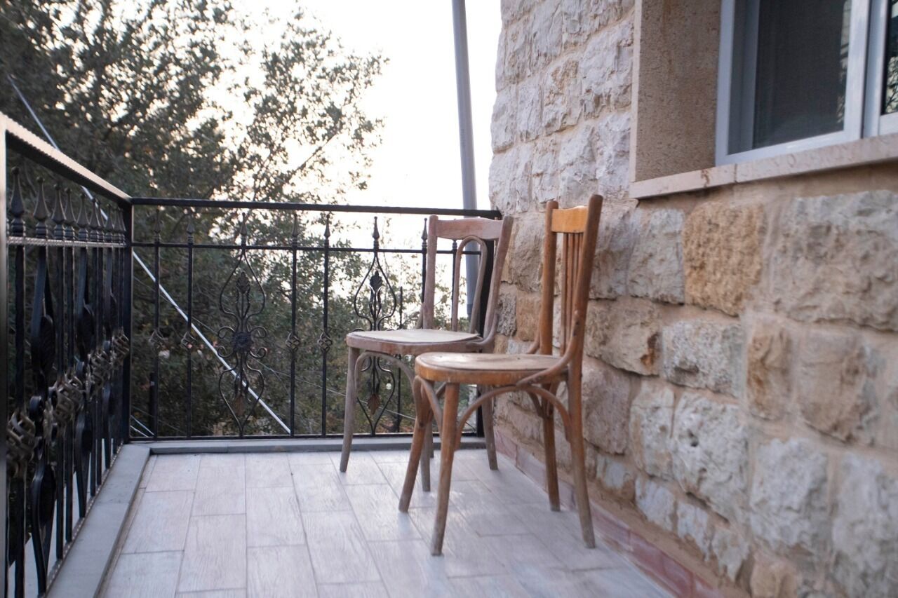 Un balcón con dos sillas de madera y un muro de piedra.
