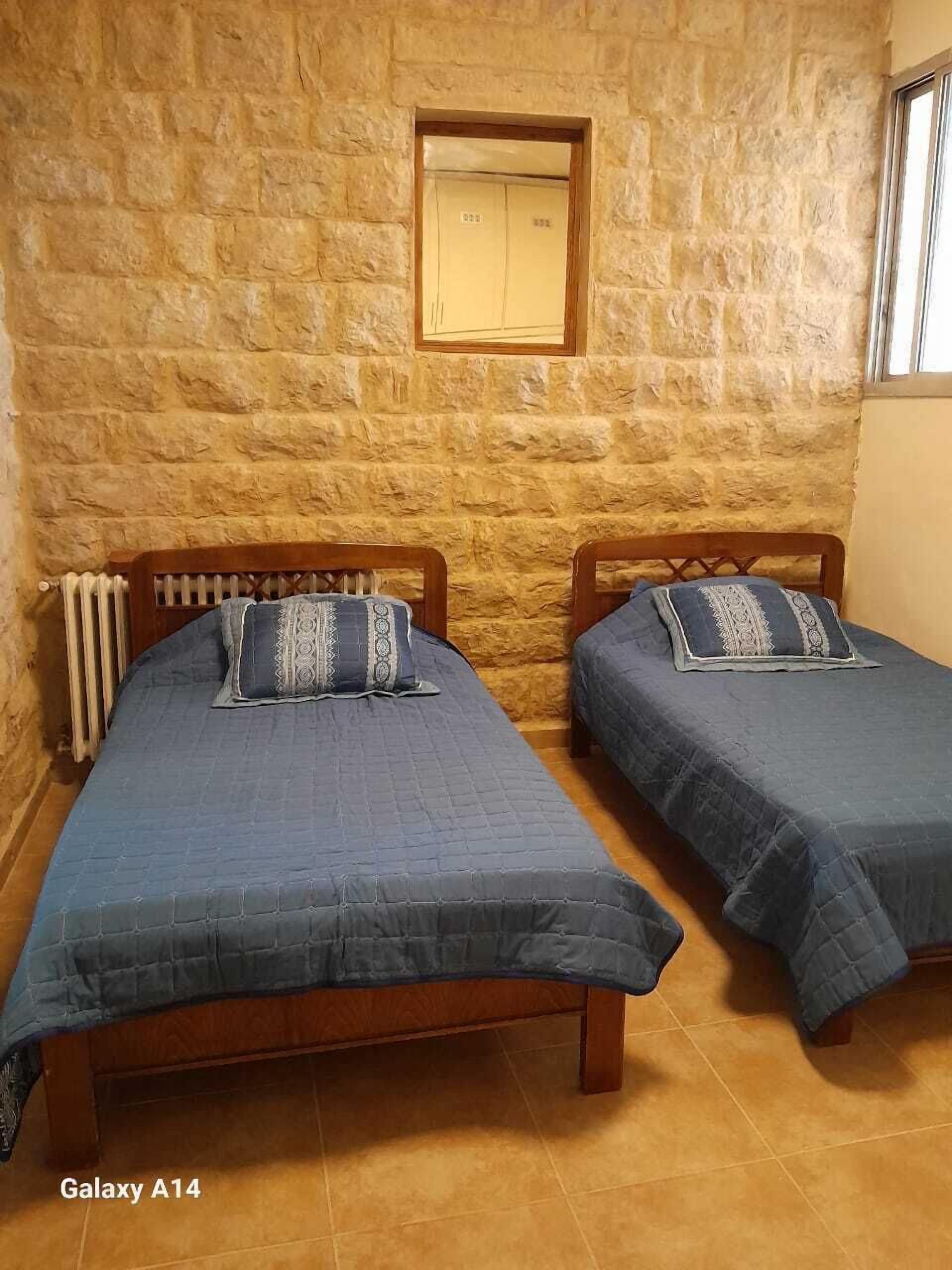 A room with two wooden beds, a stone wall, a radiator, and a window.