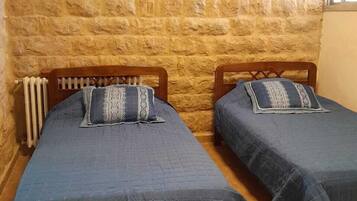 A room with two wooden beds, a stone wall, a radiator, and a window.