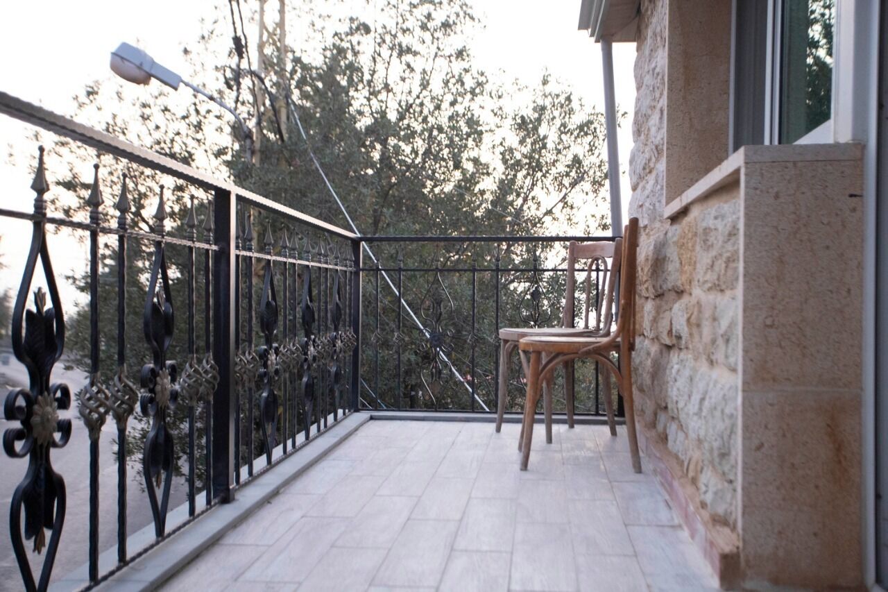 Un balcón con barandilla de hierro forjado, una silla de madera y un muro de piedra.