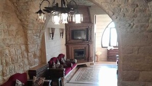 A stone-walled living room with a fireplace, red sofa, patterned rug, and a chandelier. - Chill Inn by Hansa  (Chemlane)