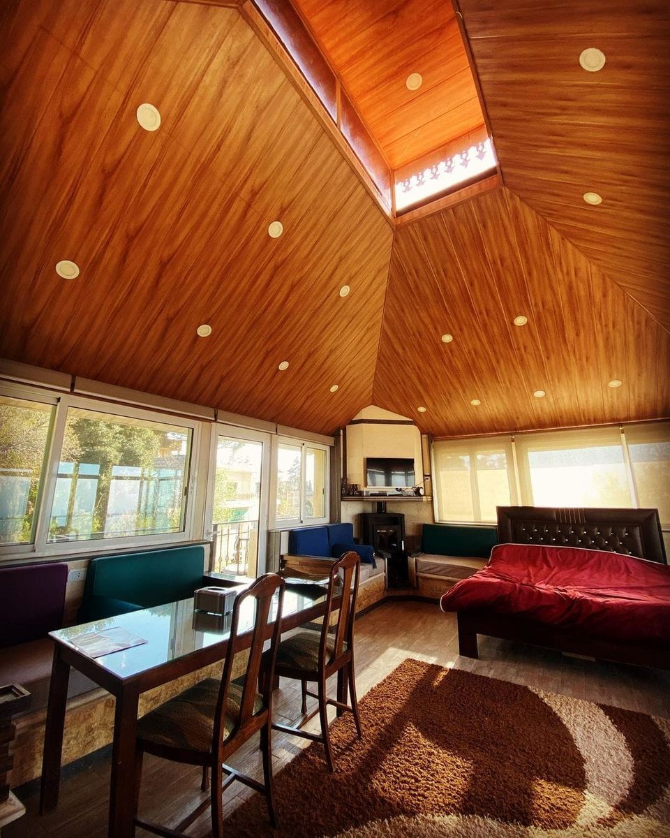 Une pièce spacieuse avec un plafond haut, des poutres apparentes, une table à manger avec des chaises, un canapé et un lit.