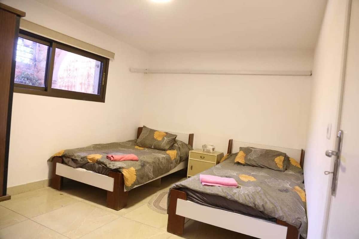 A small, clean room with two single beds, a nightstand, and a window.