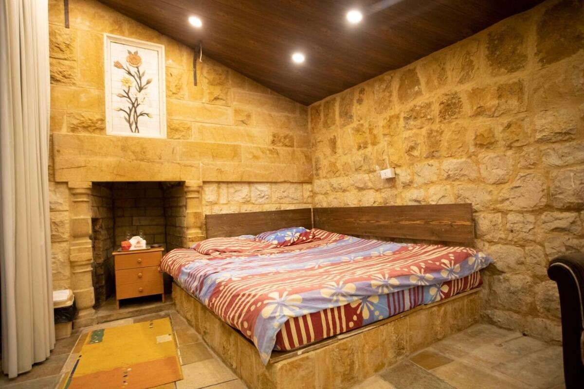 A bedroom with a stone wall, a wooden headboard, a bed with a floral bedspread, a nightstand, and a fireplace.