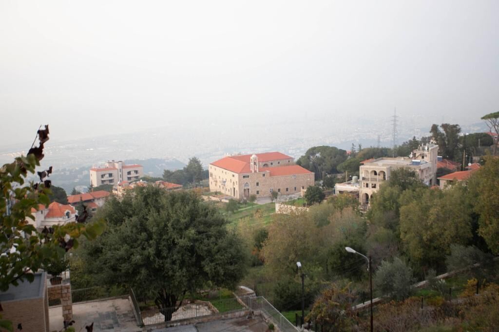 A view of a town with various buildings, including a prominent building with a red roof and a smaller building with a white facade.