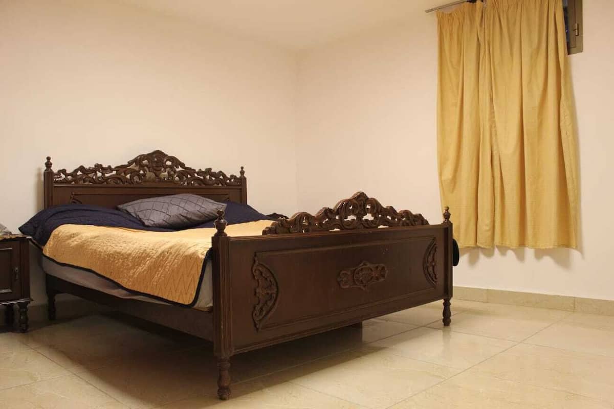 A wooden bed with a headboard, a nightstand, and a yellow curtain.