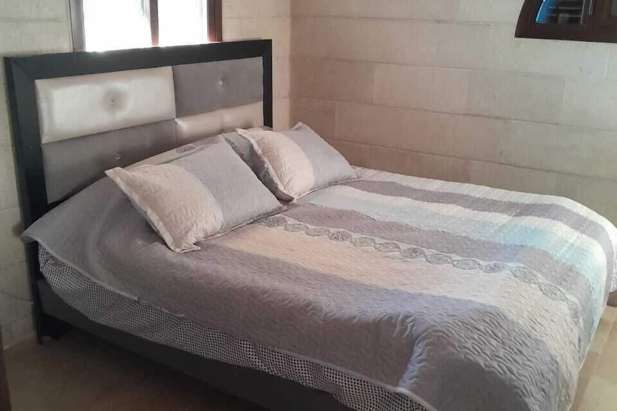 A bed with a headboard, a window with blinds, and a wall with a built-in shelf.