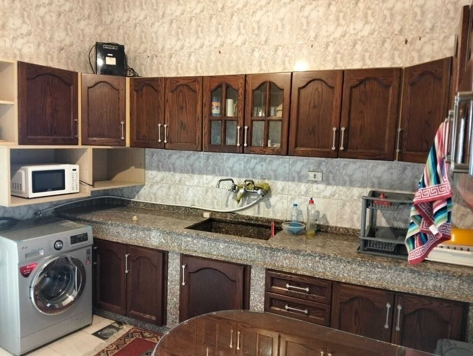 Una cocina compacta con muebles de madera, microondas integrado, lavabo y lavadora.