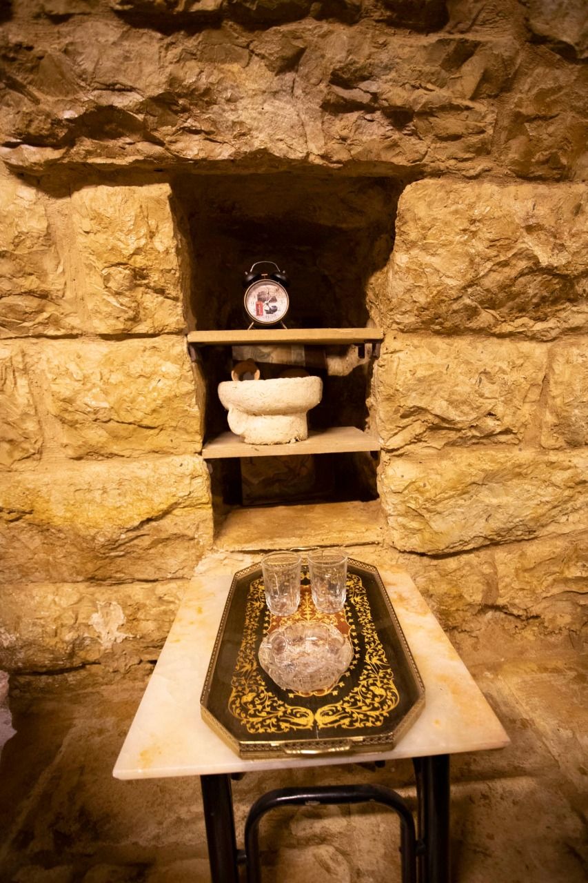 A stone wall with a shelf holding a clock, a stone basin, and a tray with glasses and bottles.