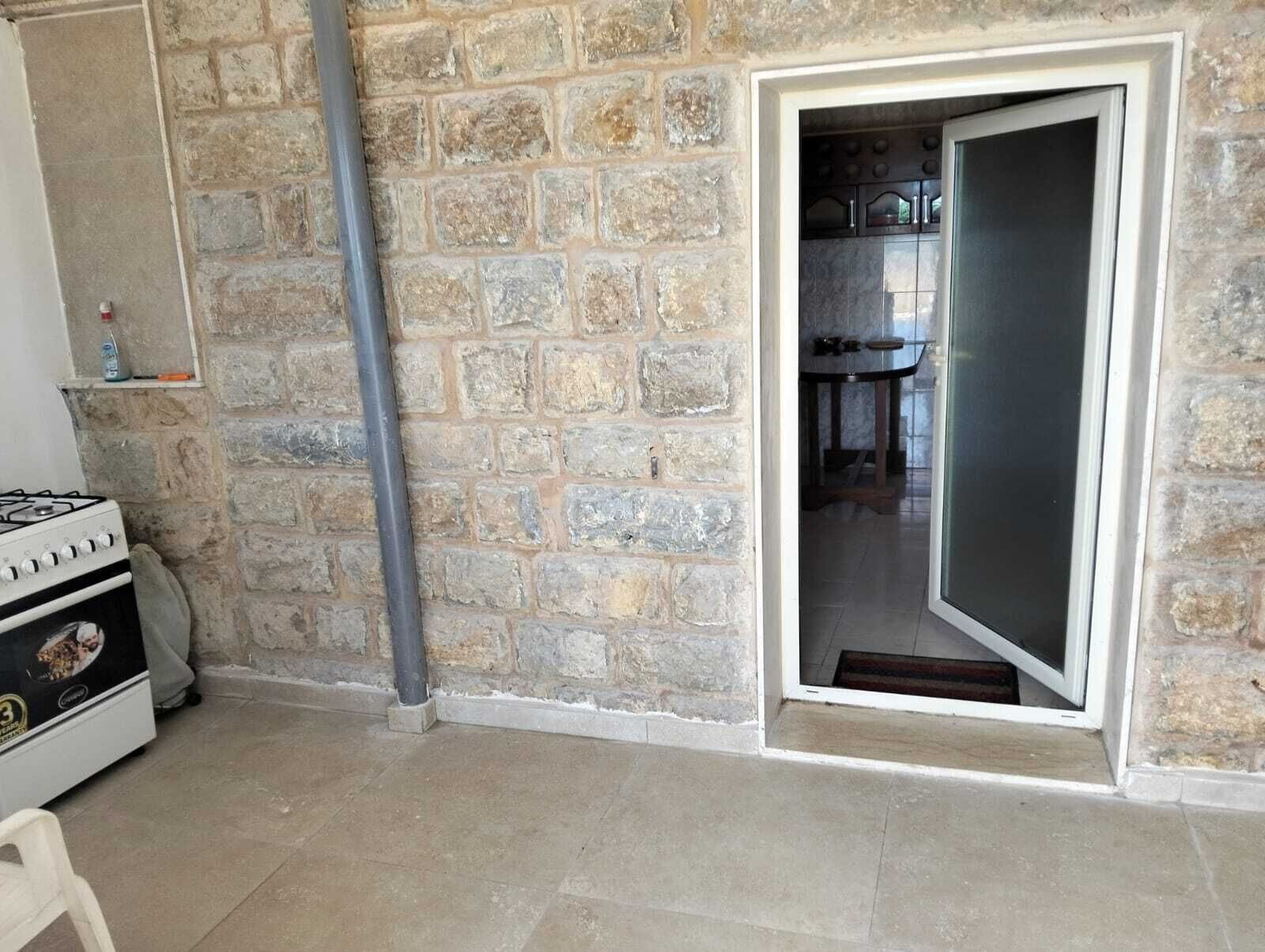 A kitchen with a gas stove, a stone wall, and a door leading to a dining area.