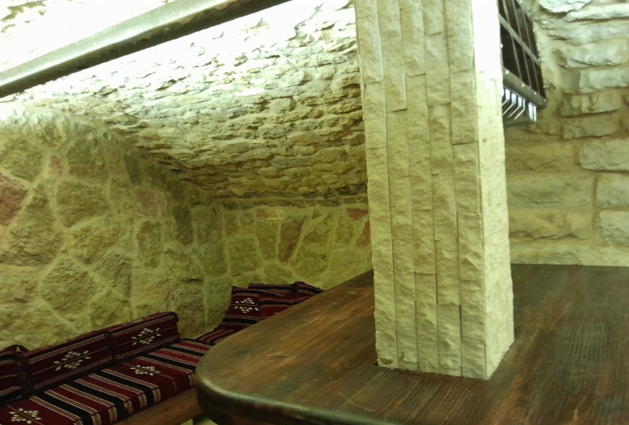 A stone-walled room with a wooden bench and a patterned rug.