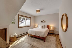 A bedroom with a large bed, a window with a view of a snowy landscape, a wooden floor, and a small bedside table with a lamp. - Downtown Modern Frisco Getaway (Frisco)