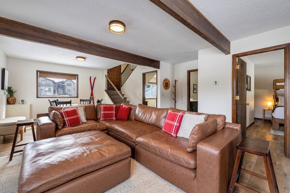 A spacious living room with a large brown leather sectional sofa, a wooden staircase, and a view of the outside. - Downtown Modern Frisco Getaway (Frisco)
