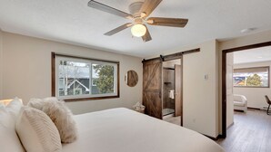A bedroom with a large bed, a ceiling fan, a window, and a sliding door leading to a bathroom. - Downtown Modern Frisco Getaway (Frisco)