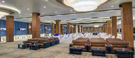 A spacious hall with rows of brown leather sofas and tables, a large chandelier, and a blue curtain backdrop.