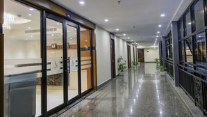 A hotel corridor with glass doors, a reception area, and a polished floor. - The Bindal Hotel (Jamshedpur)