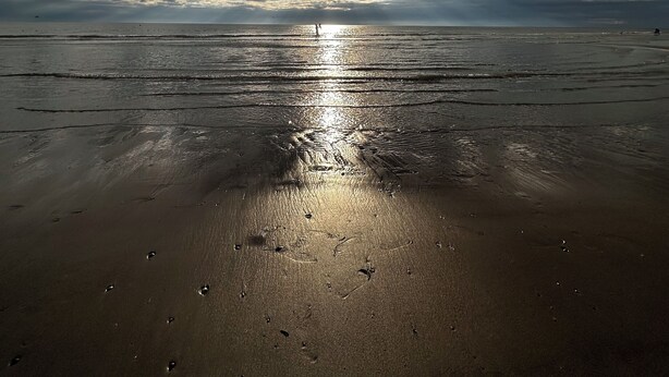 Een strand bij zonsondergang, nat zand en voetafdrukken.