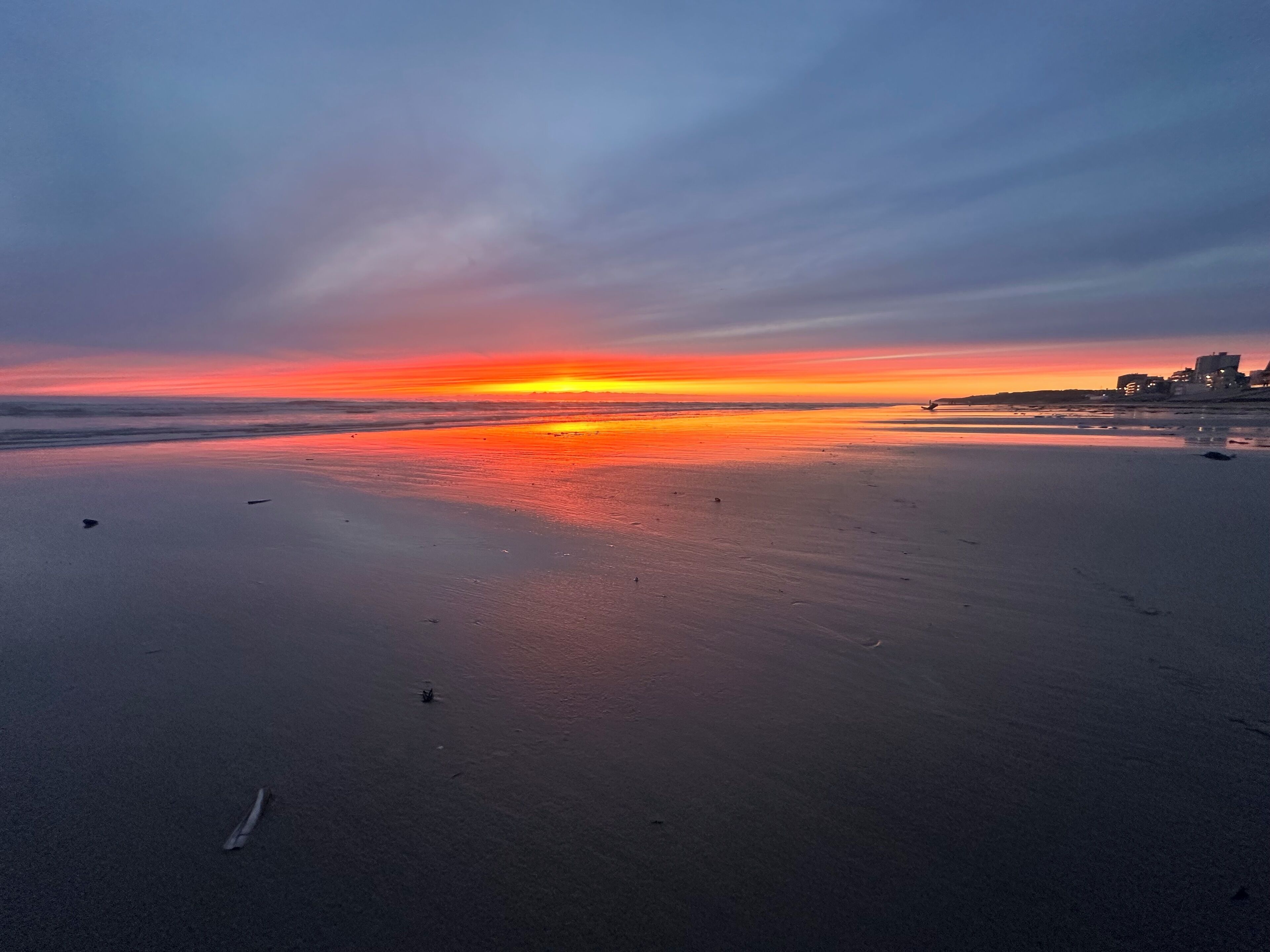 Ein Strand bei Sonnenuntergang mit ruhiger See und einer fernen Stadtansicht.
