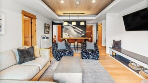 Una sala moderna con un sofá, dos sillones estampados, una mesita de centro, una zona de comedor con mesa y sillas, y un televisor montado en la pared.