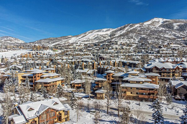 Un pueblo cubierto de nieve en la montaña, con varios edificios, incluyendo hoteles y viviendas, bajo un cielo azul despejado.