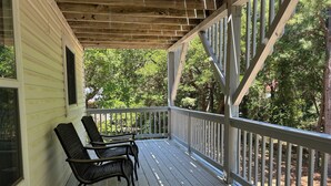 A covered porch with two chairs, a wooden ceiling, and a view of trees. - Spacious 3BR/3BA Beach House on Quiet Wooded Lot – Minutes from the Ocean (Kitty Hawk)