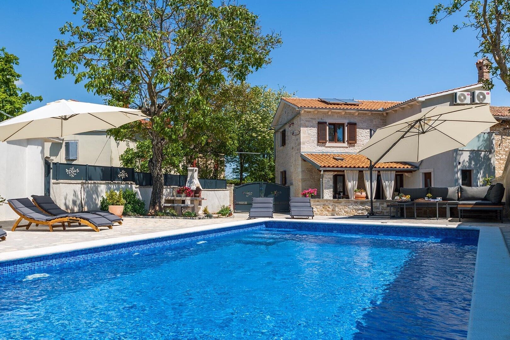 A swimming pool with lounge chairs, a covered seating area, and a stone building with a tiled roof.