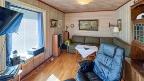 Ein gemütliches Wohnzimmer mit Sofa, Sessel, Tisch mit Fernbedienung, Fernseher und Bücherregal.