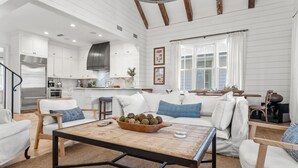 Un salón amplio con una mesa de centro de madera, sofás blancos y una cocina al fondo.