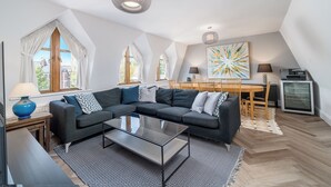 A modern living room with a sectional sofa, a glass coffee table, and a dining area with a wooden table and chairs. - Chic 2BR Battersea Flat - Terrace & Pet-Friendly (London)