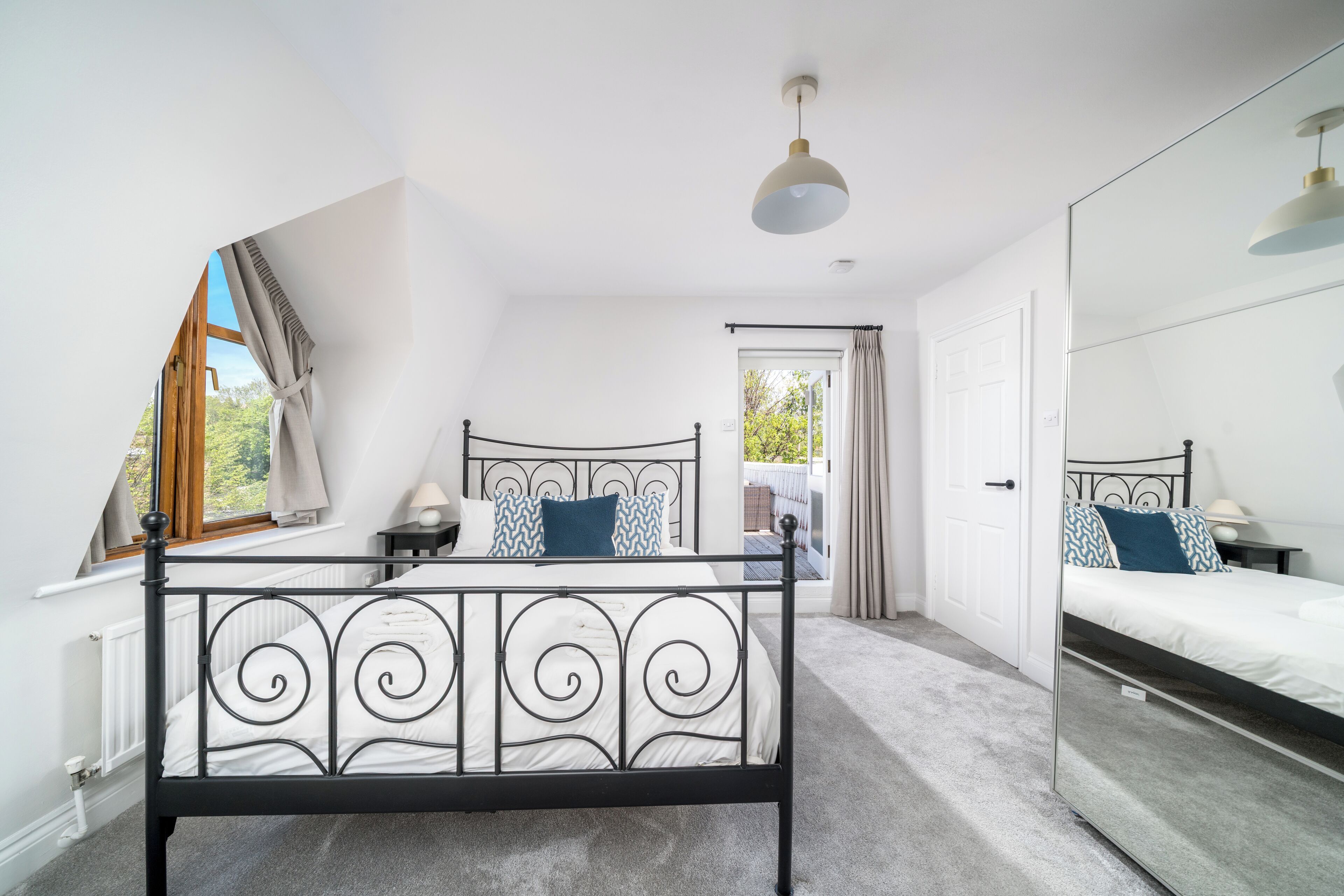 A bedroom with a black metal bed frame, a large mirror, a window with curtains, and a ceiling light.