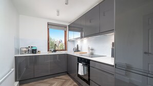 A modern kitchen with grey cabinets, a built-in oven, and a window with a city view. - Chic 2BR Battersea Flat - Terrace & Pet-Friendly (London)