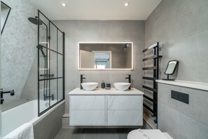 A modern bathroom with a glass-enclosed shower, a large mirror, and a white vanity with two sinks.