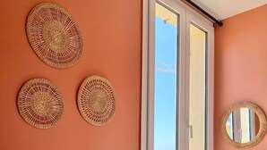 A bedroom with a bed, a window with a view of the sea, and three woven wall decorations. - Vue mer - Monaco - clim (Cap-d'Ail)
