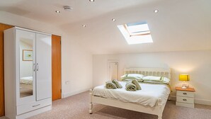 A bedroom with a bed, a wardrobe, a nightstand, and a skylight. - Stable Barn Apartment at Bodmin Moor (St Breward)
