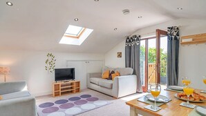 A modern living room with a sofa, TV, and dining area with breakfast. - Stable Barn Apartment at Bodmin Moor (St Breward)