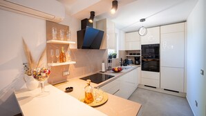 Une cuisine moderne avec des meubles blancs, un four encastré et un îlot central doté d’un évier et d’un plan de travail.